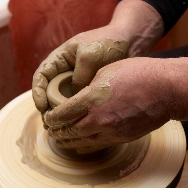 Two hands making a small pot on a pottery wheel